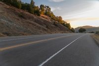 a person riding a motorcycle on a road at dusk with hills and bushes in the background