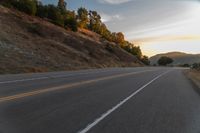 a person riding a motorcycle on a road at dusk with hills and bushes in the background