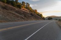 a person riding a motorcycle on a road at dusk with hills and bushes in the background