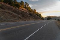 a person riding a motorcycle on a road at dusk with hills and bushes in the background