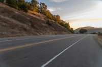 a person riding a motorcycle on a road at dusk with hills and bushes in the background