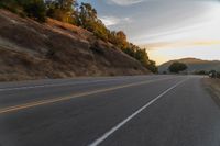 a person riding a motorcycle on a road at dusk with hills and bushes in the background