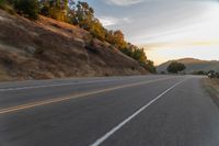 a person riding a motorcycle on a road at dusk with hills and bushes in the background