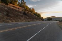 a person riding a motorcycle on a road at dusk with hills and bushes in the background