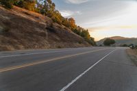 a person riding a motorcycle on a road at dusk with hills and bushes in the background