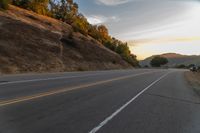 a person riding a motorcycle on a road at dusk with hills and bushes in the background