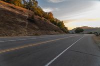 a person riding a motorcycle on a road at dusk with hills and bushes in the background