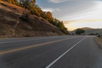 a person riding a motorcycle on a road at dusk with hills and bushes in the background