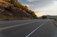 a person riding a motorcycle on a road at dusk with hills and bushes in the background