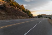 a person riding a motorcycle on a road at dusk with hills and bushes in the background