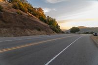 a person riding a motorcycle on a road at dusk with hills and bushes in the background