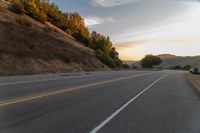 a person riding a motorcycle on a road at dusk with hills and bushes in the background