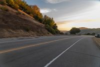 a person riding a motorcycle on a road at dusk with hills and bushes in the background