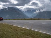 a red van is driving on the road near mountains with clouds in the sky over a valley