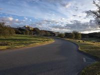 a paved road winds through an open green meadow next to the village of ancona in southern portugal