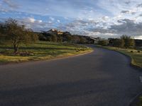 a paved road winds through an open green meadow next to the village of ancona in southern portugal