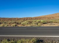 an asphalt road and two cars driving down it with a mountain in the background on the other side