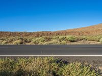 an asphalt road and two cars driving down it with a mountain in the background on the other side