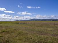 a single pole fenced in area that looks grassy and cloudy, and a hill in the distance