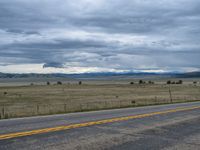 a long street passes a prairie area and mountains in the distance with heavy clouds in the sky