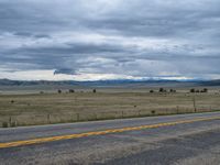 a long street passes a prairie area and mountains in the distance with heavy clouds in the sky