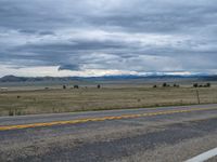 a long street passes a prairie area and mountains in the distance with heavy clouds in the sky