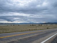 a long street passes a prairie area and mountains in the distance with heavy clouds in the sky