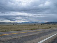 a long street passes a prairie area and mountains in the distance with heavy clouds in the sky