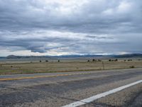 a long street passes a prairie area and mountains in the distance with heavy clouds in the sky