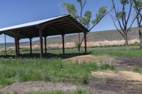 a gazebo is seen on the grass of a ranch land near trees and dirt