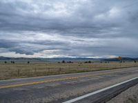 a long street passes a prairie area and mountains in the distance with heavy clouds in the sky