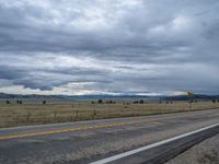 a long street passes a prairie area and mountains in the distance with heavy clouds in the sky