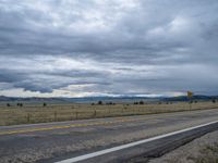 a long street passes a prairie area and mountains in the distance with heavy clouds in the sky