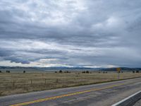 a long street passes a prairie area and mountains in the distance with heavy clouds in the sky