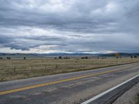 a long street passes a prairie area and mountains in the distance with heavy clouds in the sky