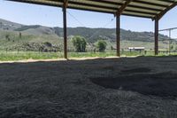 this is an outdoor horse stable with dirt, hills, and a field in the background