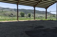 this is an outdoor horse stable with dirt, hills, and a field in the background