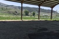 this is an outdoor horse stable with dirt, hills, and a field in the background