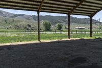 this is an outdoor horse stable with dirt, hills, and a field in the background