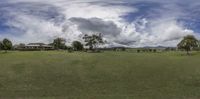 a view of a farm with cows grazing in it and clouds overhead above it that are overcasted and slightly dark