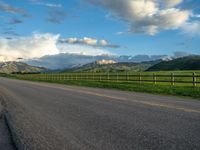 the road is empty during the day and has mountains in the distance as well as a fence