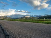 the road is empty during the day and has mountains in the distance as well as a fence