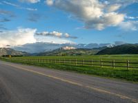 the road is empty during the day and has mountains in the distance as well as a fence