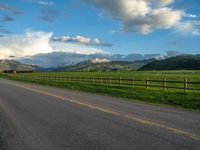 the road is empty during the day and has mountains in the distance as well as a fence