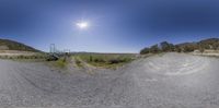 a 360 - angle picture of a dirt road near mountains and green grass with a bright sun in the distance