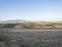 a field with dry grass near telephone wires in the distance, and hills, behind them