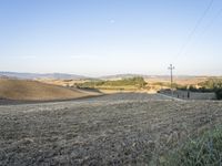 a field with dry grass near telephone wires in the distance, and hills, behind them