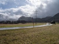 an empty field next to power lines on a cloudy day in the countryside with snow capped mountains