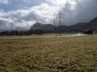 an empty field next to power lines on a cloudy day in the countryside with snow capped mountains