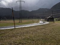 an empty field next to power lines on a cloudy day in the countryside with snow capped mountains